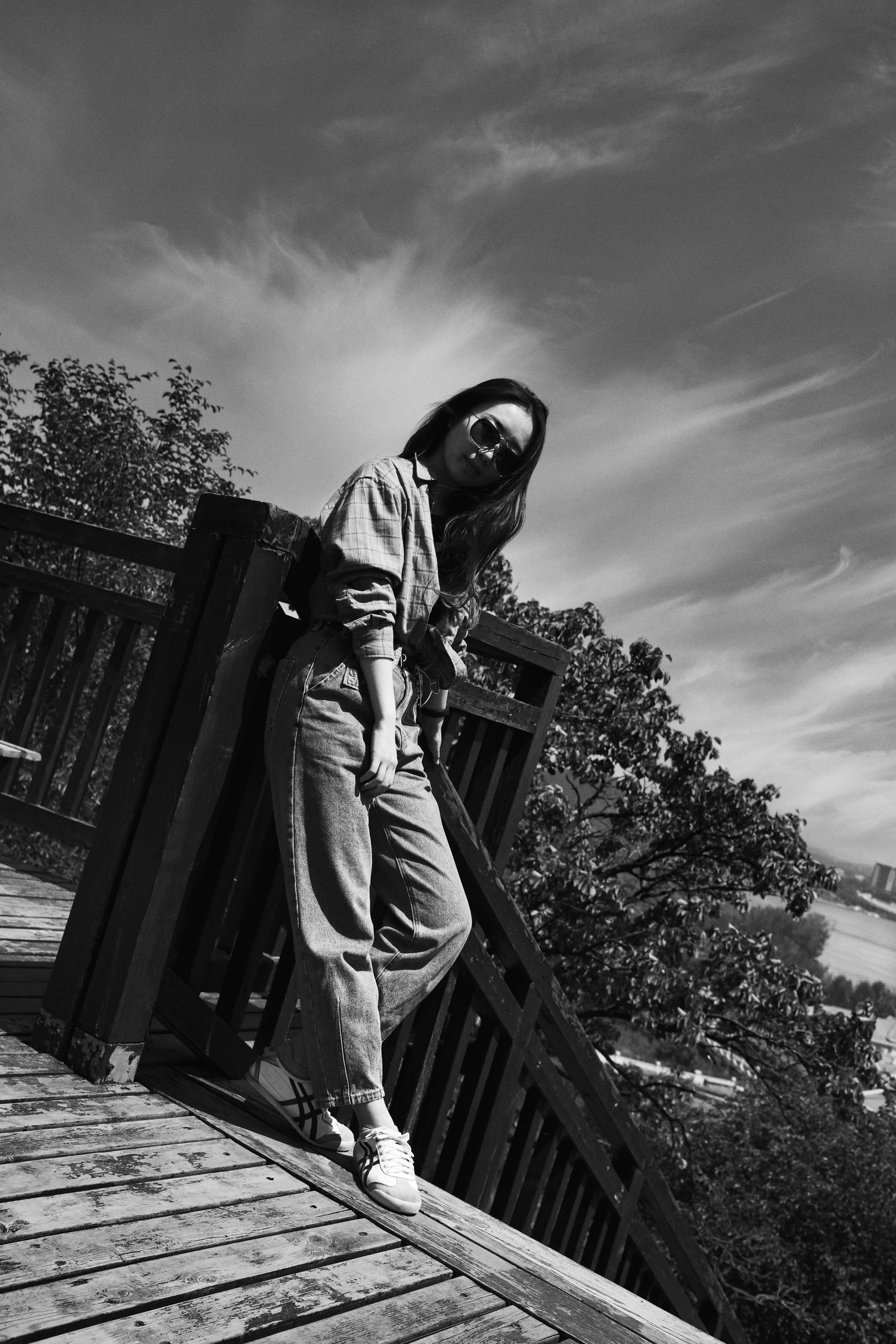 grayscale photo of person in hoodie and pants standing on wooden dock